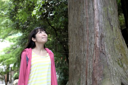 Foto de Mujer asiática de pie cerca de árbol y mirando hacia arriba en parque - Imagen libre de derechos