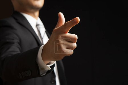Photo for Businessman in suit showing pointing gesture on black background - Royalty Free Image