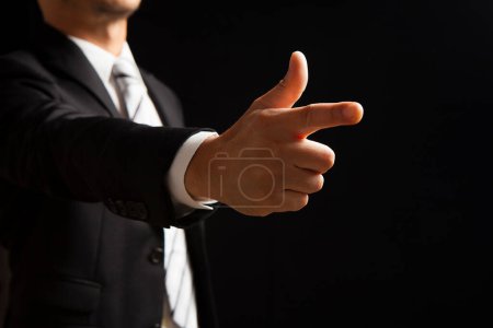 Photo for Businessman in suit showing pointing gesture on black background - Royalty Free Image