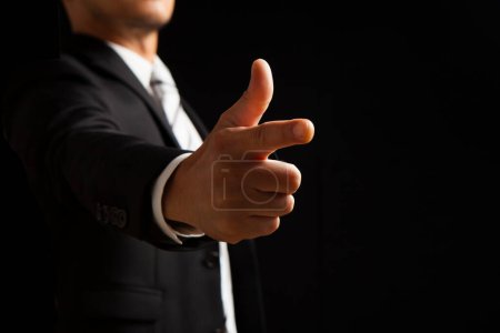 Téléchargez les photos : Homme d'affaires en costume montrant geste pointu sur fond noir - en image libre de droit