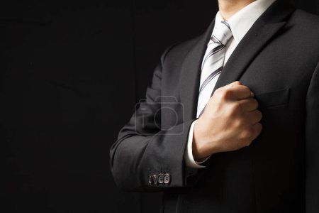 Photo for Businessman in black suit showing trust by put his fist on left chest on black background - Royalty Free Image