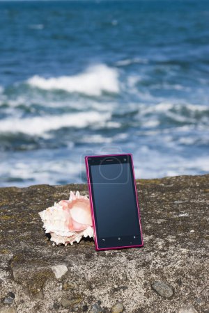 Téléchargez les photos : Smartphone avec écran blanc et coquillage sur la plage, espace de copie - en image libre de droit