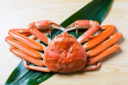 close up view of red snow crab and green leaf on wooden table