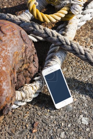 Téléchargez les photos : Téléphone portable, vieille ancre rouillée et grande corde sur la plage de la mer - en image libre de droit