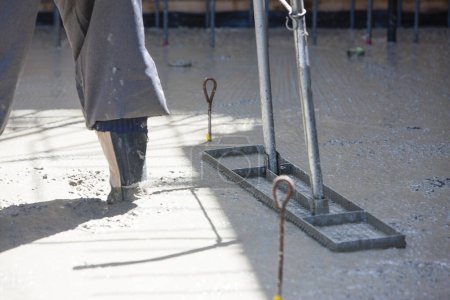 trabajador suaviza un sitio de construcción con una herramienta de regla para la colocación de losas de pavimentación