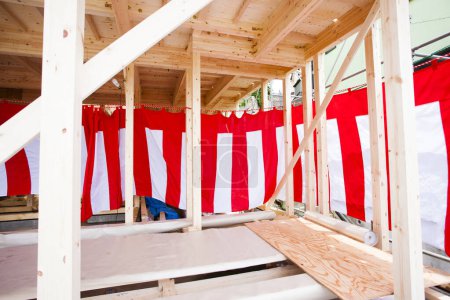 New house under construction. Wooden beams decorated with red and white striped textile for building completion ceremony