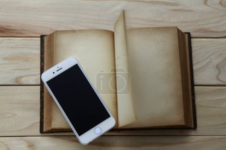 Téléchargez les photos : Téléphone portable avec écran noir et vieux livre avec des pages blanches sur fond en bois - en image libre de droit