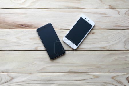 Foto de Dos teléfonos inteligentes con pantallas en blanco en escritorio de madera. - Imagen libre de derechos
