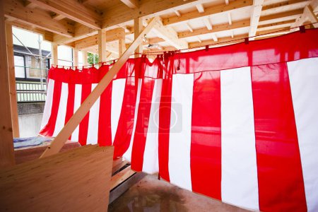 Téléchargez les photos : Nouvelle maison en construction. Poutres en bois décorées de textile rayé rouge et blanc pour la cérémonie d'achèvement de la construction - en image libre de droit
