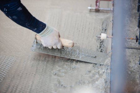 Téléchargez les photos : Travailleur utilisant une spatule pour niveler le ciment sur le chantier - en image libre de droit