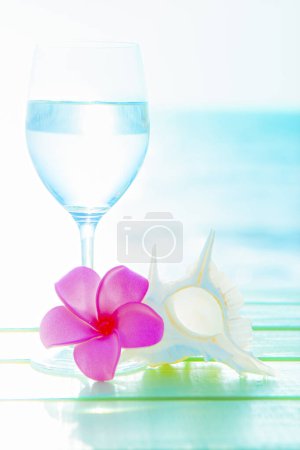 Photo for Summer background with plumeria flower, shell and wineglass with water on the beach - Royalty Free Image