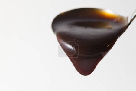 Foto de Salsa oscura gruesa que fluye de cucharón sobre un fondo blanco - Imagen libre de derechos