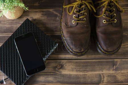 Téléchargez les photos : Smartphone moderne avec des bottes en cuir sur une table en bois. - en image libre de droit
