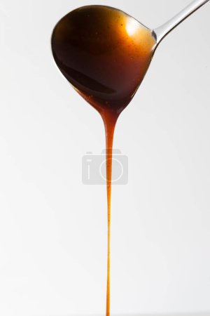 Photo for Thick dark sauce flowing from ladle on a white background - Royalty Free Image