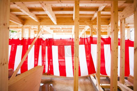 New house under construction. Wooden beams decorated with red and white striped textile for building completion ceremony