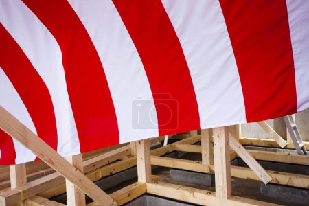 Foto de Nueva casa en construcción. Vigas de madera decoradas con textiles a rayas rojas y blancas para la ceremonia de finalización del edificio - Imagen libre de derechos