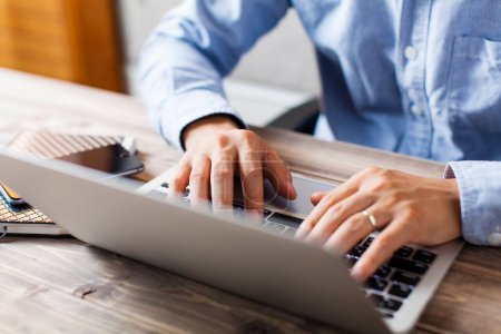 Téléchargez les photos : Jeune homme d'affaires utilisant un ordinateur portable tout en étant assis sur une table en bois - en image libre de droit