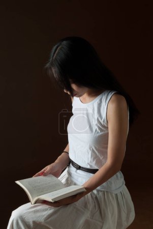 Téléchargez les photos : Portrait de jeune femme asiatique lisant un vieux livre en chambre noire - en image libre de droit
