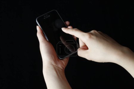 Téléchargez les photos : Mains féminines tenant smartphone sur fond noir - en image libre de droit