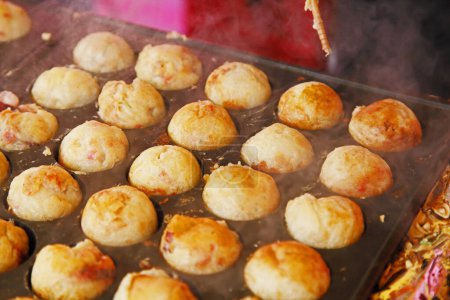 cooking Takoyaki, ball-shaped Japanese snacks made of a wheat flour-based batter and cooked in a special molded pan