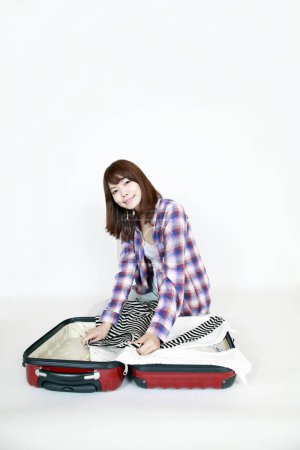 Téléchargez les photos : Portrait de belle jeune femme asiatique en chemise à carreaux avec valise de voyage sur fond blanc - en image libre de droit