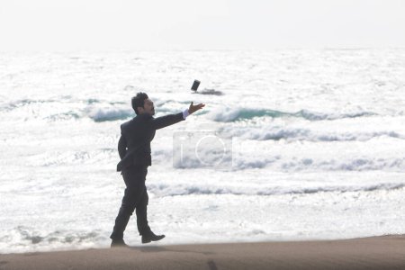 Foto de Joven asiático hombre de negocios tirar teléfono hasta mientras caminando en playa - Imagen libre de derechos