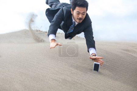 Foto de Asiático hombre de negocios tratando de coger el teléfono que está atrapado en la arena - Imagen libre de derechos