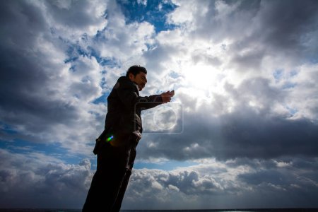 Téléchargez les photos : Asiatique homme d'affaires en costume avec téléphone mobile sur ciel bleu - en image libre de droit