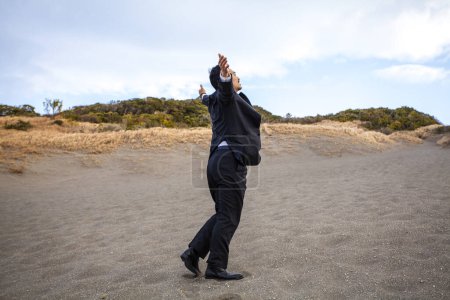 Foto de Asiático hombre de negocios levantando brazos mientras caminando en arenosa playa - Imagen libre de derechos