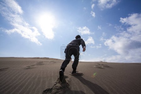 Photo for Asian businessman walking on sandy beach, rear view - Royalty Free Image