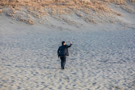 Foto de Asiático hombre de negocios en traje formal caminar a lo largo de la playa de arena, vista trasera - Imagen libre de derechos