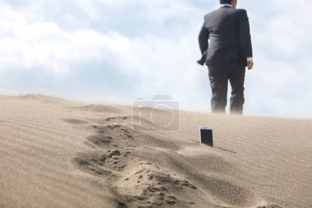Téléchargez les photos : Section basse de l'homme d'affaires marchant à travers le téléphone qui est coincé dans le sable - en image libre de droit