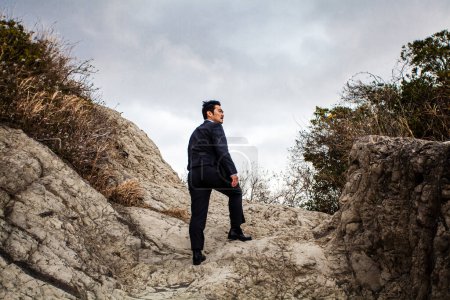 Foto de Asiático hombre de negocios caminar en rocoso playa - Imagen libre de derechos