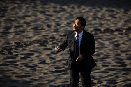 Téléchargez les photos : Asiatique homme d'affaires en costume formel marche le long de la plage de sable - en image libre de droit