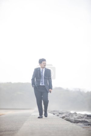 Photo for Asian businessman in a black suit walks near sea coast - Royalty Free Image