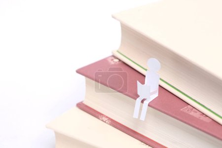 Foto de Pila de libros con una figura humana de papel aislada sobre fondo blanco - Imagen libre de derechos
