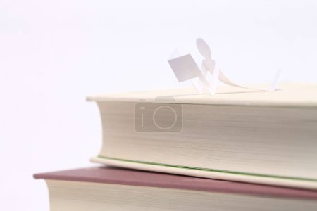 Photo for Stack of books with a paper human figure isolated on white background - Royalty Free Image