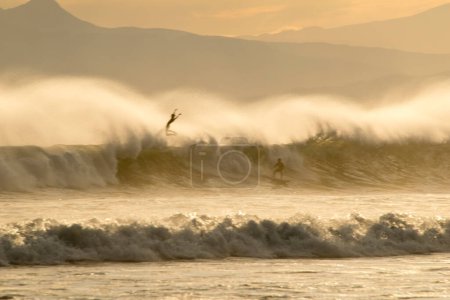 Foto de Surfistas montando una ola de mar al atardecer, ocio activo - Imagen libre de derechos