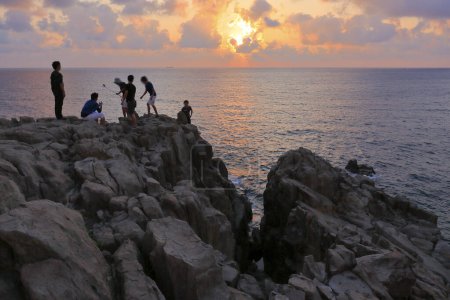 Foto de Personas de pie en la costa rocosa y mirando al hermoso atardecer vista del mar - Imagen libre de derechos