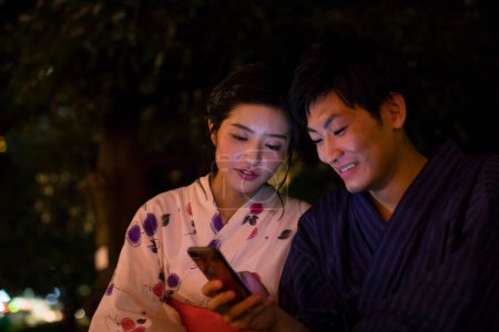 Téléchargez les photos : Jeune couple japonais en kimono traditionnel prenant selfie sur smartphone dans le parc du soir - en image libre de droit
