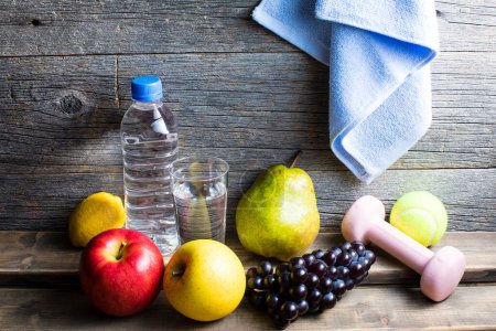 Foto de Estilo de vida saludable. Botella de agua, toalla y frutas sobre fondo de madera - Imagen libre de derechos