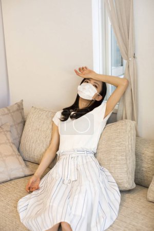 Téléchargez les photos : Asiatique jeune femme portant masque protecteur couché fatigué sur canapé à la maison - en image libre de droit