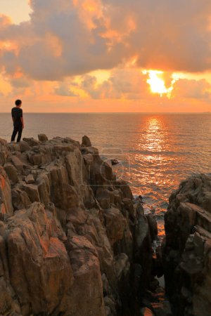 Foto de Hombre de pie sobre rocas y disfrutando de la hermosa puesta de sol sobre el mar - Imagen libre de derechos