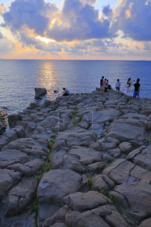 Téléchargez les photos : Touristes debout sur des rochers et profitant d'un magnifique coucher de soleil sur la mer - en image libre de droit