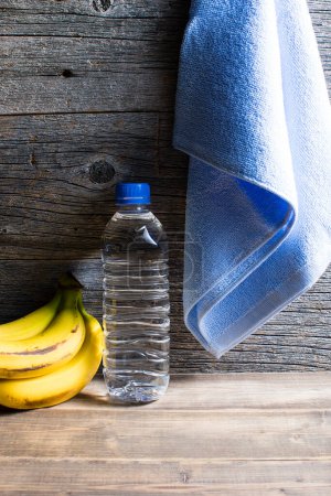 Téléchargez les photos : Mode de vie sain. Bouteille d'eau, serviette et bananes sur fond en bois - en image libre de droit