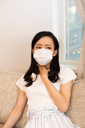 Photo for Asian young woman wearing protective face mask lying tired on sofa at home - Royalty Free Image