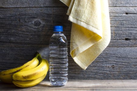 Téléchargez les photos : Mode de vie sain. Bouteille d'eau, serviette et bananes sur fond en bois - en image libre de droit