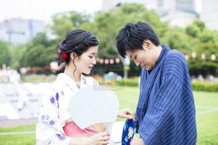 Téléchargez les photos : Jeune couple japonais portant kimono traditionnel et tenant les fans asiatiques dans le parc - en image libre de droit