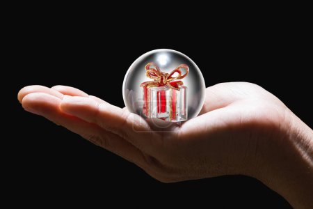 Téléchargez les photos : Main masculine tenant une boule de verre avec cadeau de Noël à l'intérieur - en image libre de droit