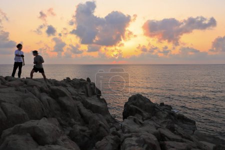 Photo for Men standing on rocks and enjoying beautiful sunset over sea - Royalty Free Image